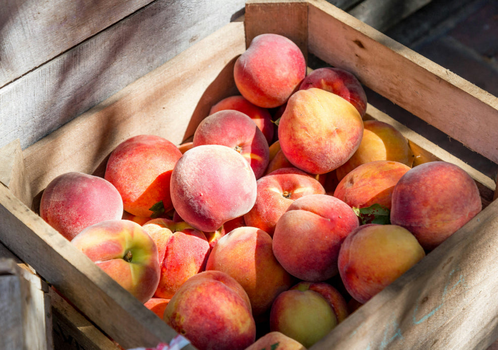 A wooden crate filled with fresh, ripe peaches under soft sunlight.