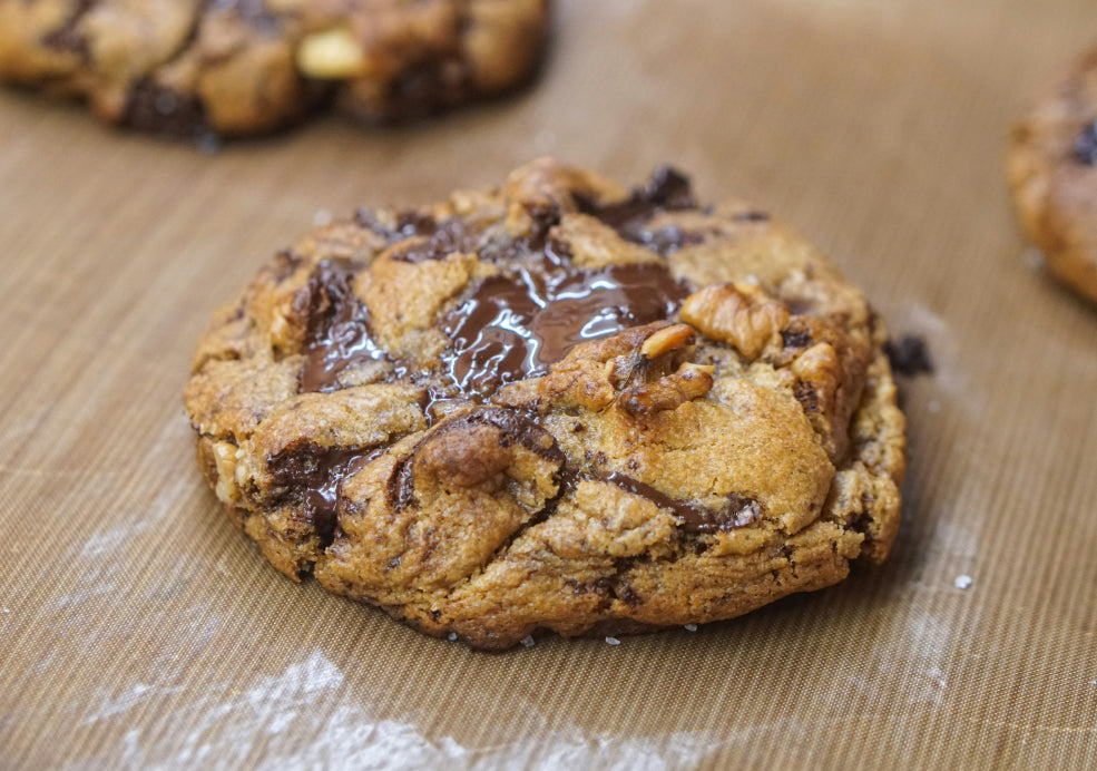 A chocolate chip cookie with melted chocolate chunks on a baking mat.