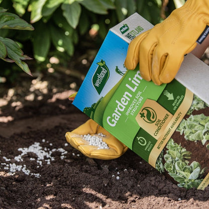 A person wearing yellow gloves is using the Westland Garden Lime 4Kg pellets to effectively reduce soil acidity.